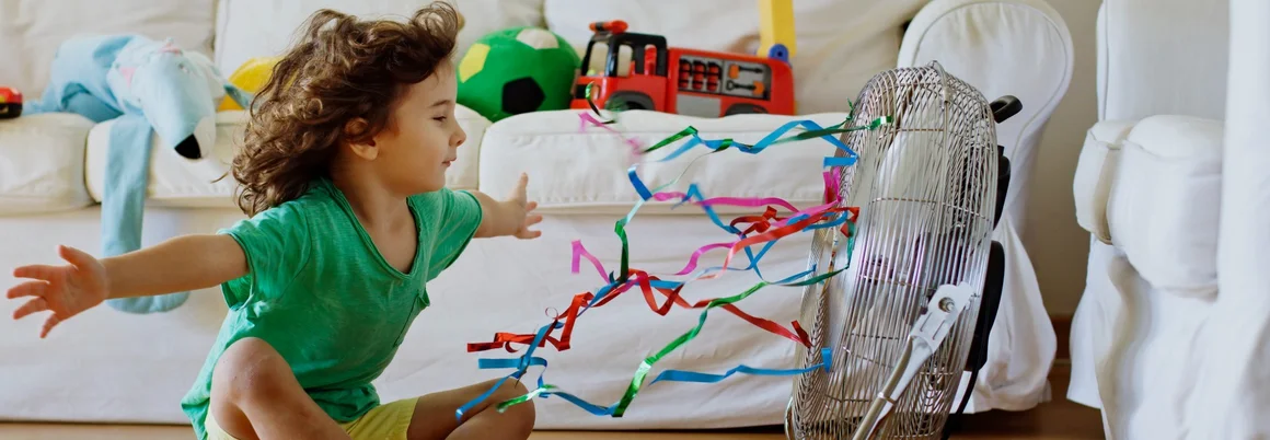 Kind spielt mit Luftschlangen am Ventilator